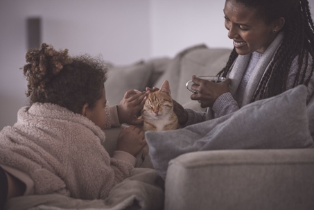 Mom and daughter under blankets petting cat